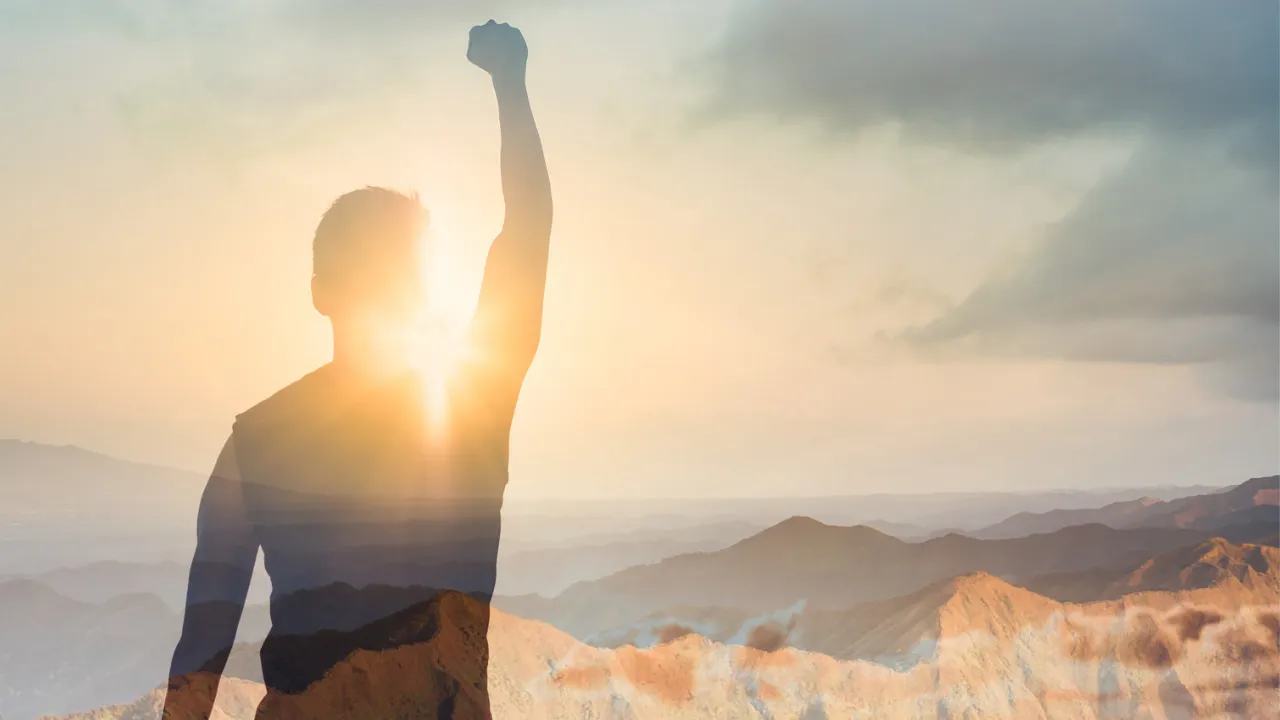 Person raising a fist on a mountain at sunrise