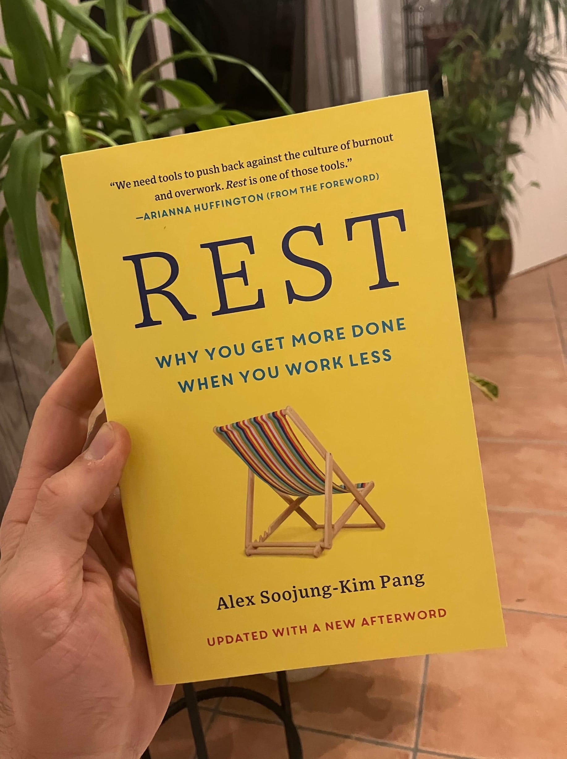 Holding the physical yellow book "Rest Why you get more done when you work less" in my hand. There is a chair on the cover page.