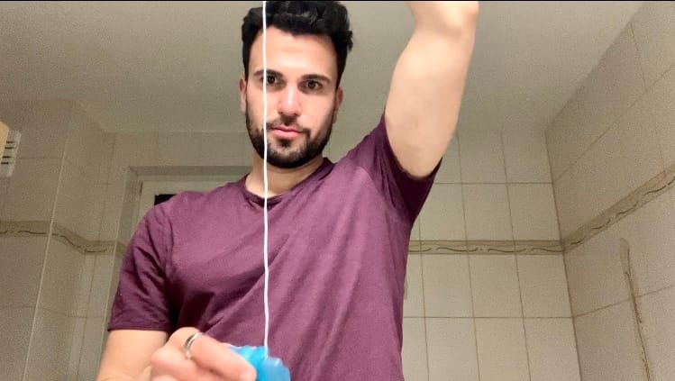 looking into the camera, purple tshirt, in the bathroom looking at the expanding floss from oral b in blue