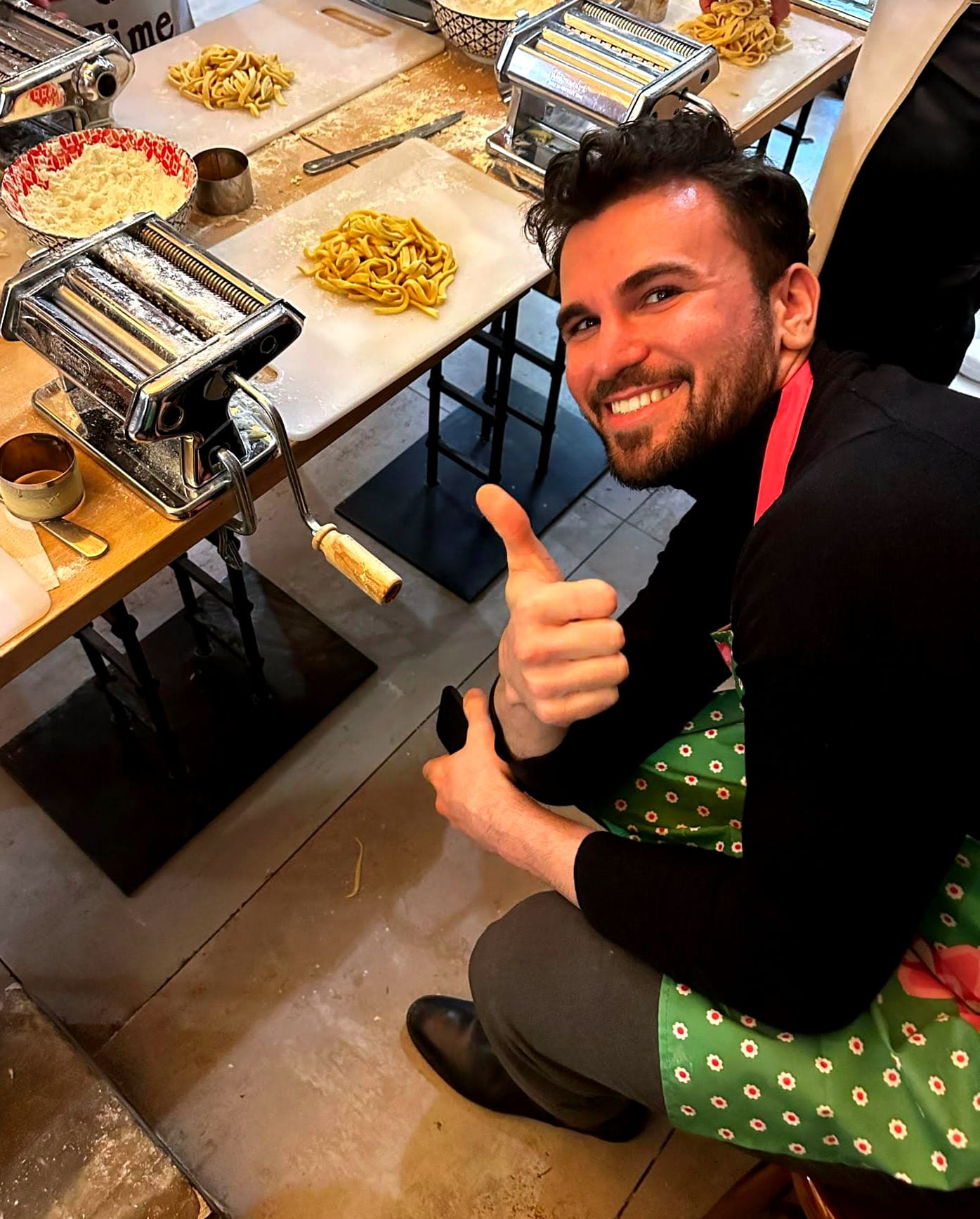 me, sitting on a chair, making pasta with the pasta machine and pasta in the background